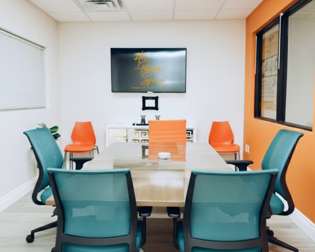Her Power Space conference room with orange accent wall, teal chairs and branded display